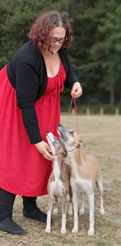 Photo of a lady with dark hair, standing with two whippets