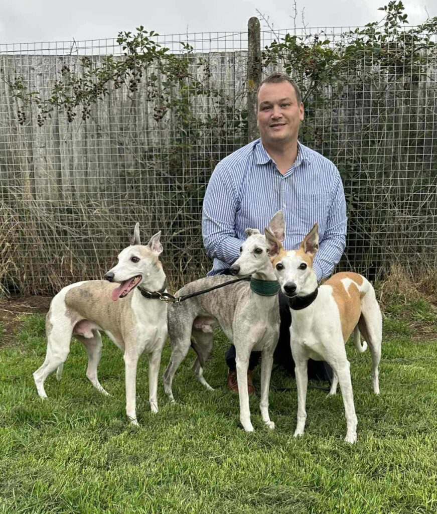 A man kneeling with three whippets